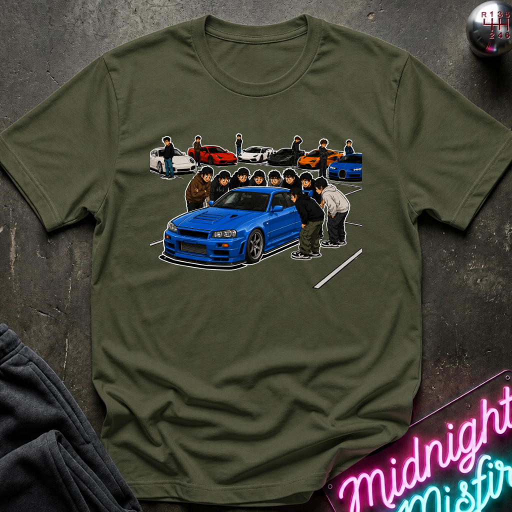 An olive green crewneck t-shirt featuring a graphic print of a blue sports car and several anime characters, styled flat on a dark textured background with a neon sign and dark sweatpants partially visible.
