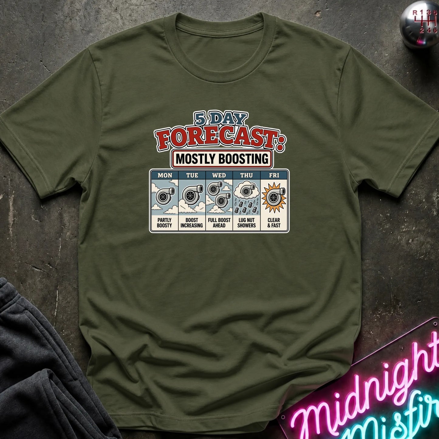 An olive green short-sleeve t-shirt with a '5 Day Forecast: Mostly Boosting' graphic print, laid flat on a dark textured surface with a neon sign and dark fabric in the foreground.