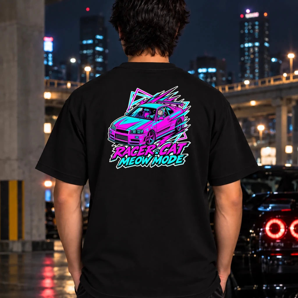 A man viewed from behind wearing a black t-shirt with a vibrant neon-style graphic of a car and the text 'RACER CAT MEOW MODE' in pink, purple, and blue. The background is a blurred nighttime city street scene with lights and buildings.