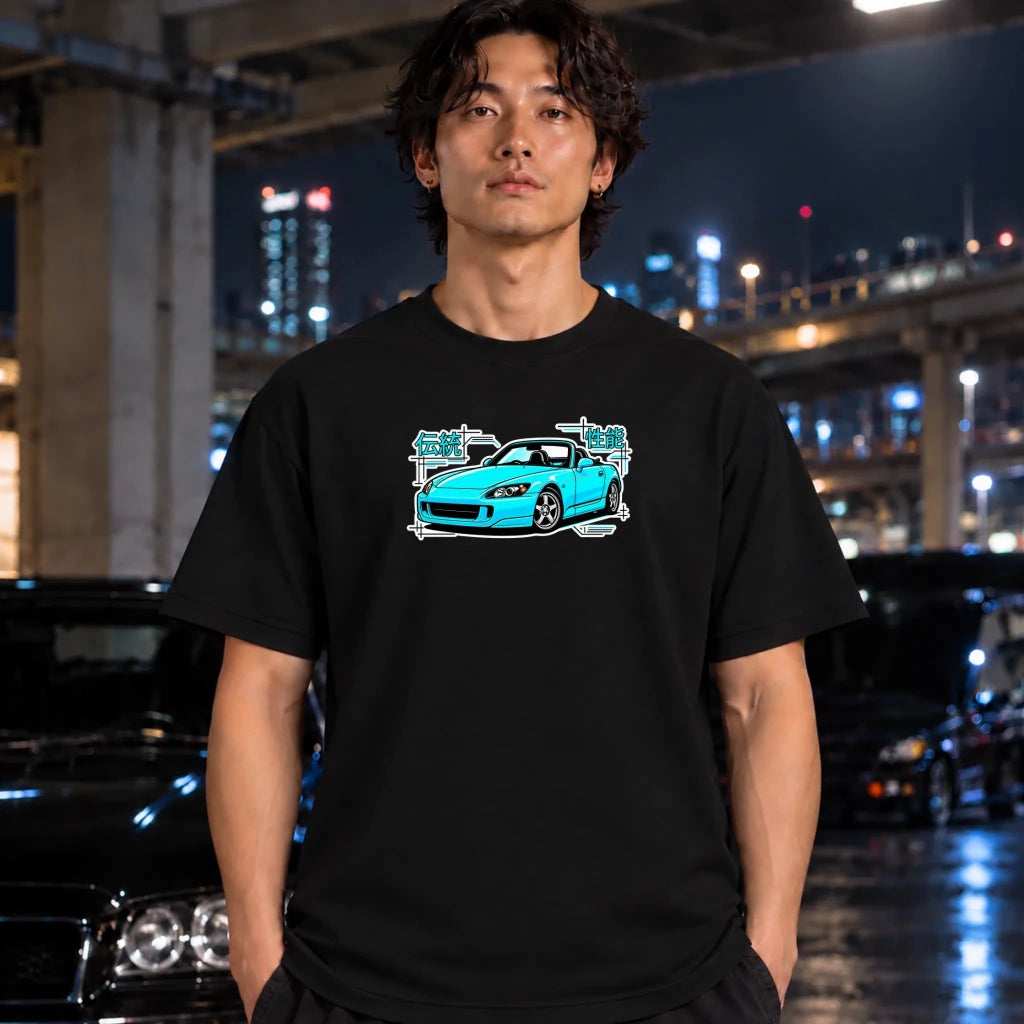 black t-shirt on a guy featuring a graphic print of a bright blue sports car with white and teal text elements. A neon sign and dark clothing are partially visible in the styled flat-lay composition.