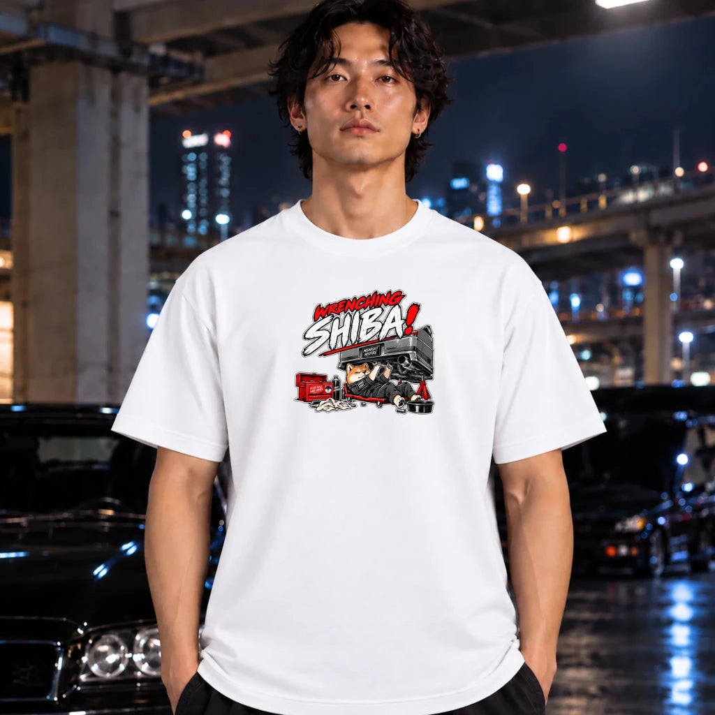 man wearing white shirt. The graphic features the text 'WRENCHING SHIBA!' in red and white comic-style lettering above an illustration of a character in a black and red vehicle.
