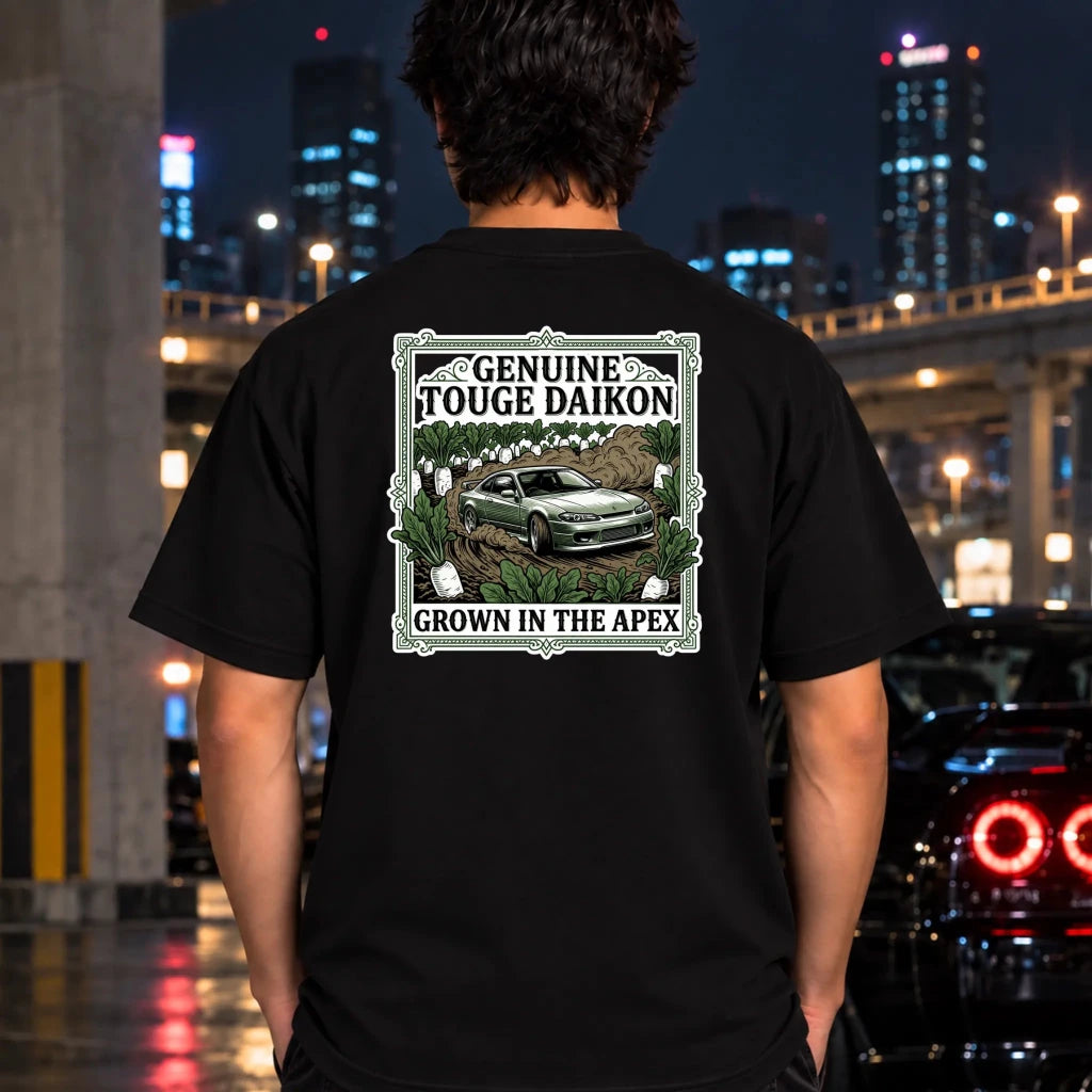 A man viewed from behind wearing a black t-shirt with a large graphic print on the back. The graphic features a green car in a field with the text 'GENUINE TOUGHE DAIKON' and 'GROWN IN THE APEX'.