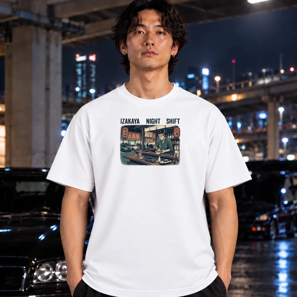 A man wearing a white graphic t-shirt with a 'Izakaya Night Shift' print, standing in a wet urban night setting with cars and city lights in the background.