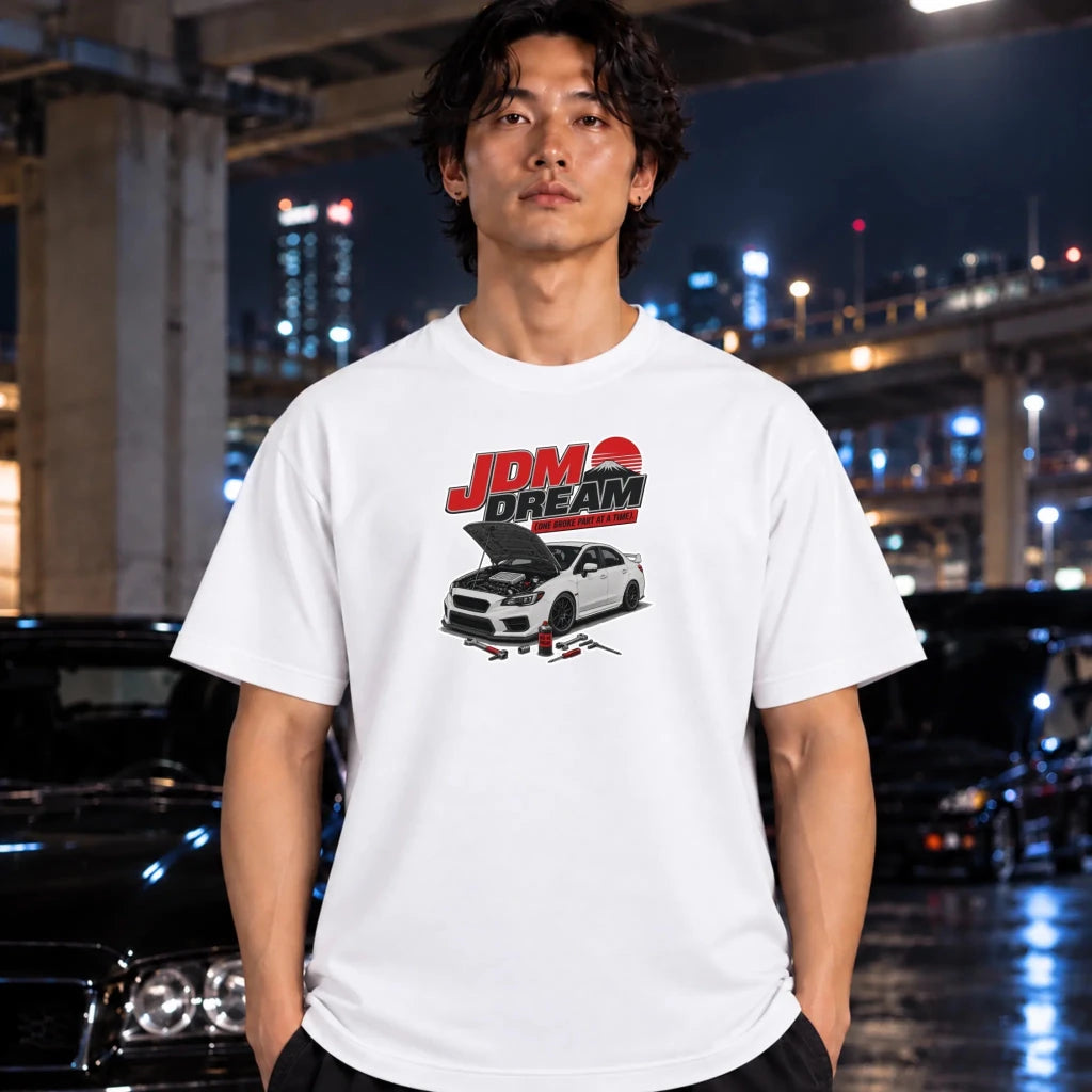 white crewneck t-shirt worn by a man, featuring a graphic of a white sports car with its hood open beneath the red and black 'JDM DREAM' text.