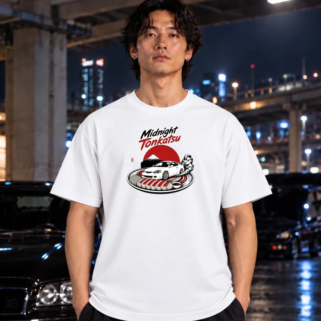 A man wearing a white graphic t-shirt with a 'Midnight Tonkatsu' car design, standing in a wet urban night environment with blurred cars and lights in the background.