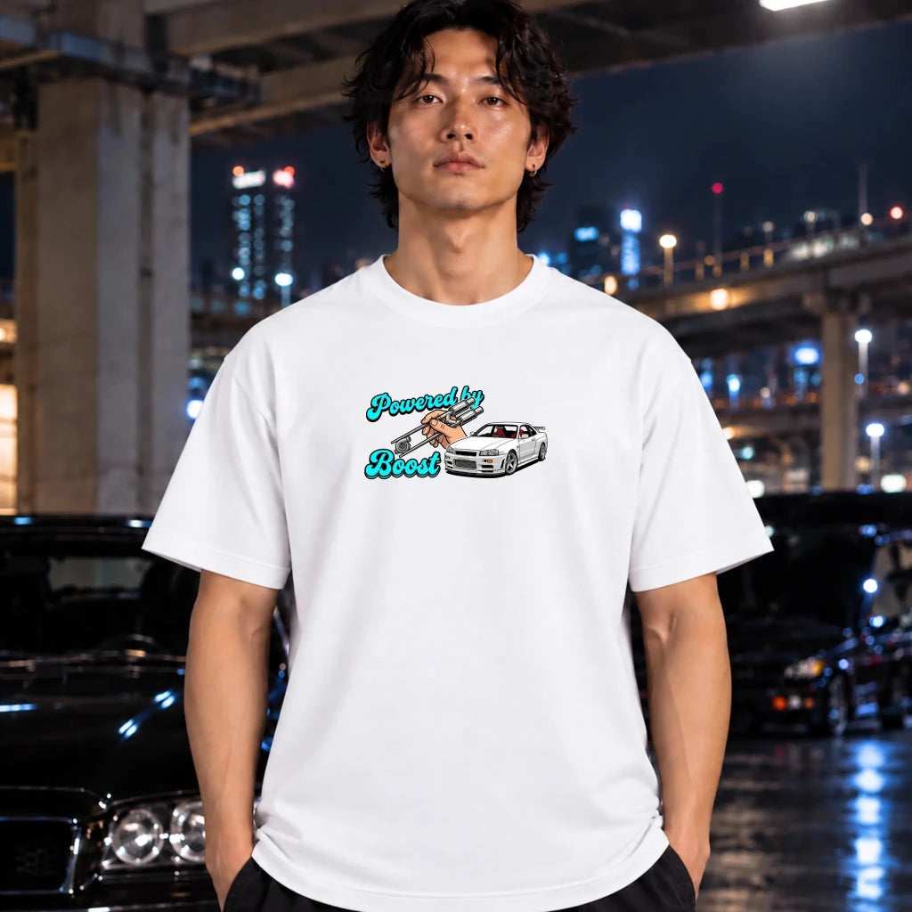 A man wearing a white graphic t-shirt with a 'Powered by boost' slogan and a car illustration, standing in front of a blurred night city background with cars.