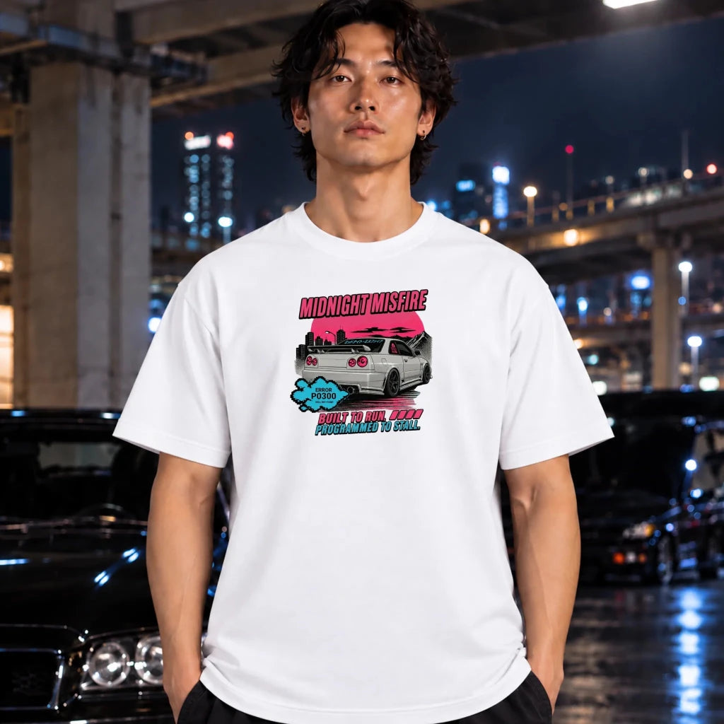 A man wearing a white graphic t-shirt with a pink and blue car design and text, standing in a wet city street at night with blurred cars and lights in the background.