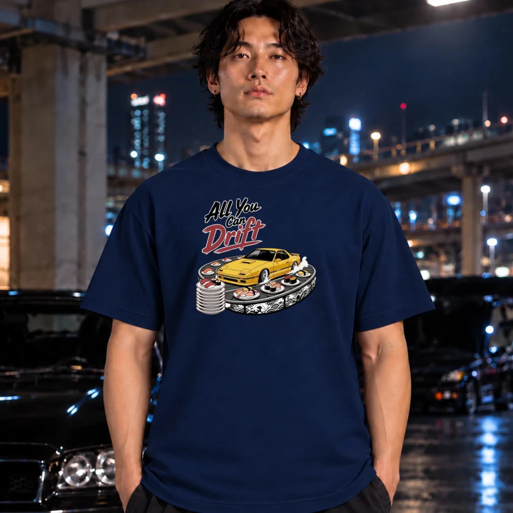 A man wearing a navy blue graphic t-shirt with a yellow drift car design, standing in a wet urban night setting with cars and city lights in the background.