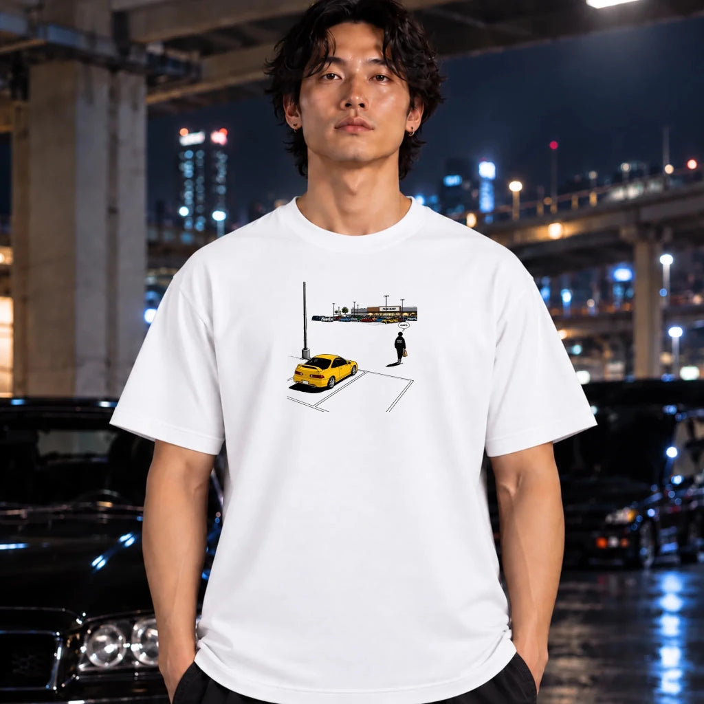 A man wearing a white graphic t-shirt with a parking spot illustration, standing in front of a blurred night city background with cars.