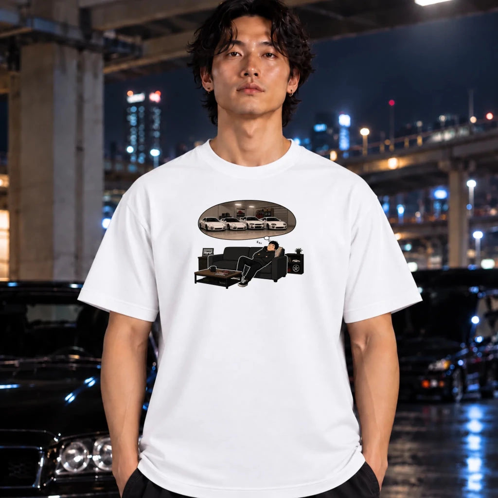 A man wearing a white graphic t-shirt with a black and white print of a man sitting on a couch under a car, set against a blurred night city background with cars and lights.