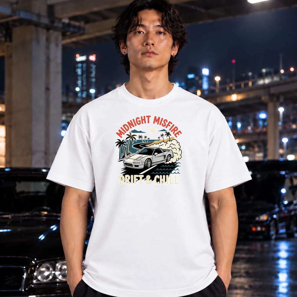 A man wearing a white graphic t-shirt with a 'Midnight Misfire Drift & Chill car design, standing in a wet urban night environment with blurred cars and city lights in the background.