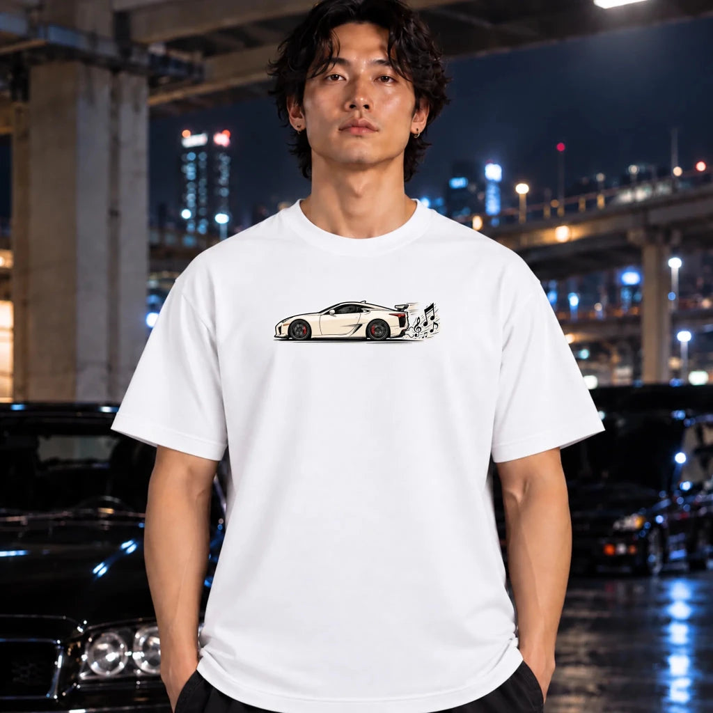 A man wearing a white short-sleeve t-shirt with a graphic of a white sports car on the chest, standing in front of a blurred night city background with cars.