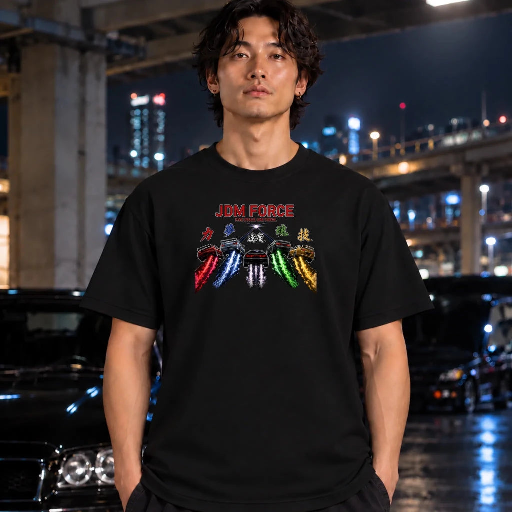 A man wearing a black t-shirt with a colorful 'JDM FORCE' graphic print, standing in a nighttime urban setting with blurred cars and city lights in the background.