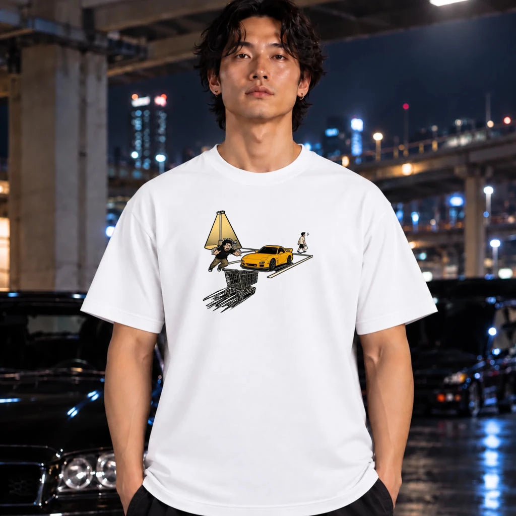 A man wearing a white graphic t-shirt with a surreal print of a yellow sports car, and a figure under a tent, posed in front of a blurred night city street background with cars.