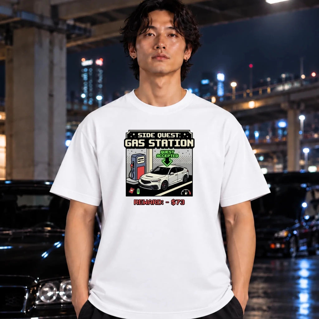 man wearing a white crewneck t-shirt featuring a retro video game style graphic of a gas station quest with a white car and a $73 reward