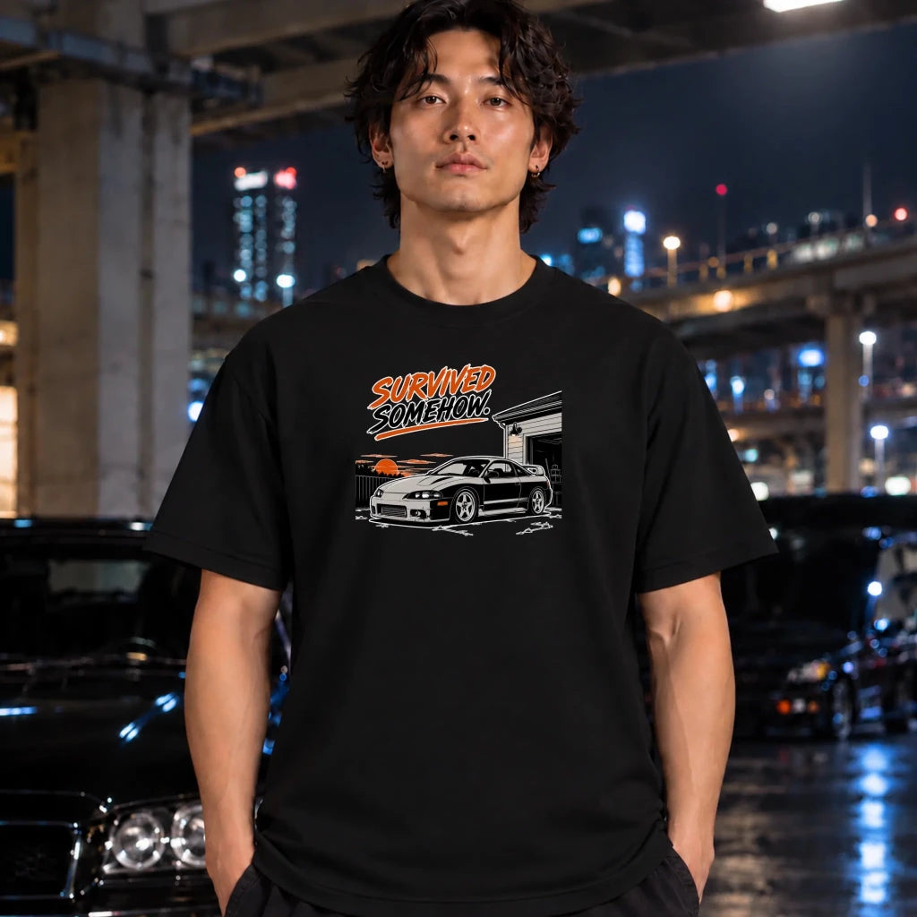 A man wearing a black graphic t-shirt with a 'Survived Someone' car design, standing in a wet urban night setting with blurred cars and city lights in the background.