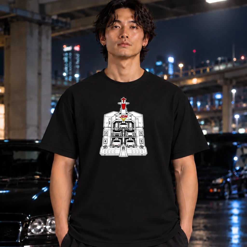 A man wearing a black t-shirt with a white and red sci-fi structure graphic on the chest, standing in a nighttime urban setting with blurred cars and city lights in the background.