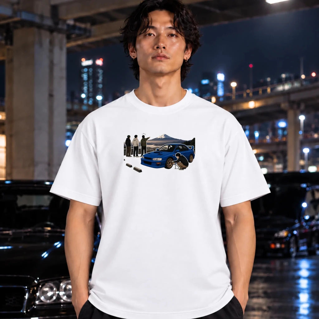 A man wearing a white graphic t-shirt with a blue sports car and scene print, standing in front of a blurred night city background with cars.
