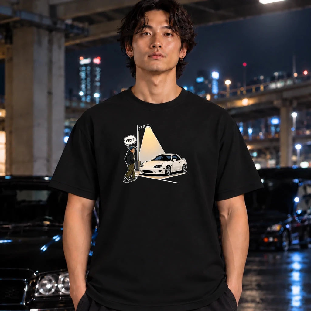 man wearing a black crewneck t-shirt, featuring a graphic print of a white sports car parked in a spot with a streetlamp shining on it and a cartoon figure with a speech bubble
