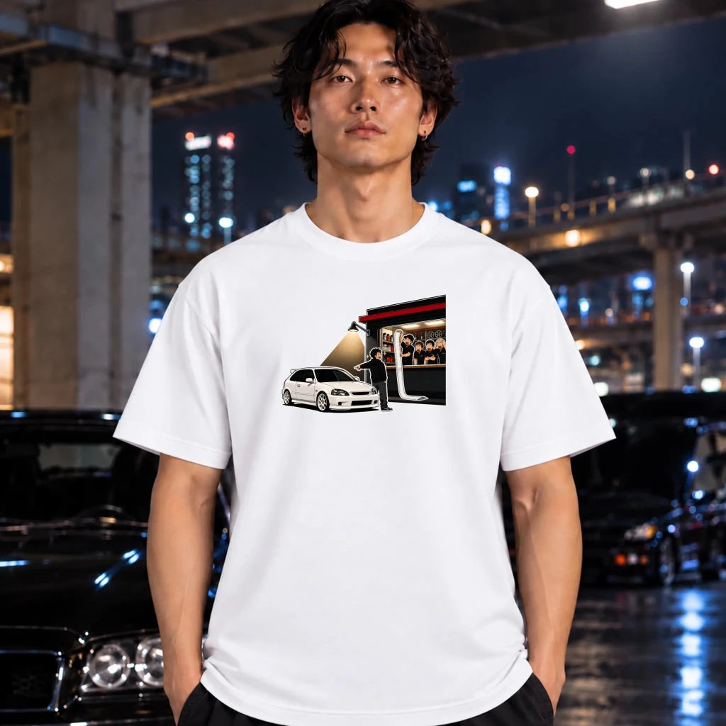 man wearing a white crewneck t-shirt, featuring a graphic print of a white car in front of a red and black trailer with people visible inside.