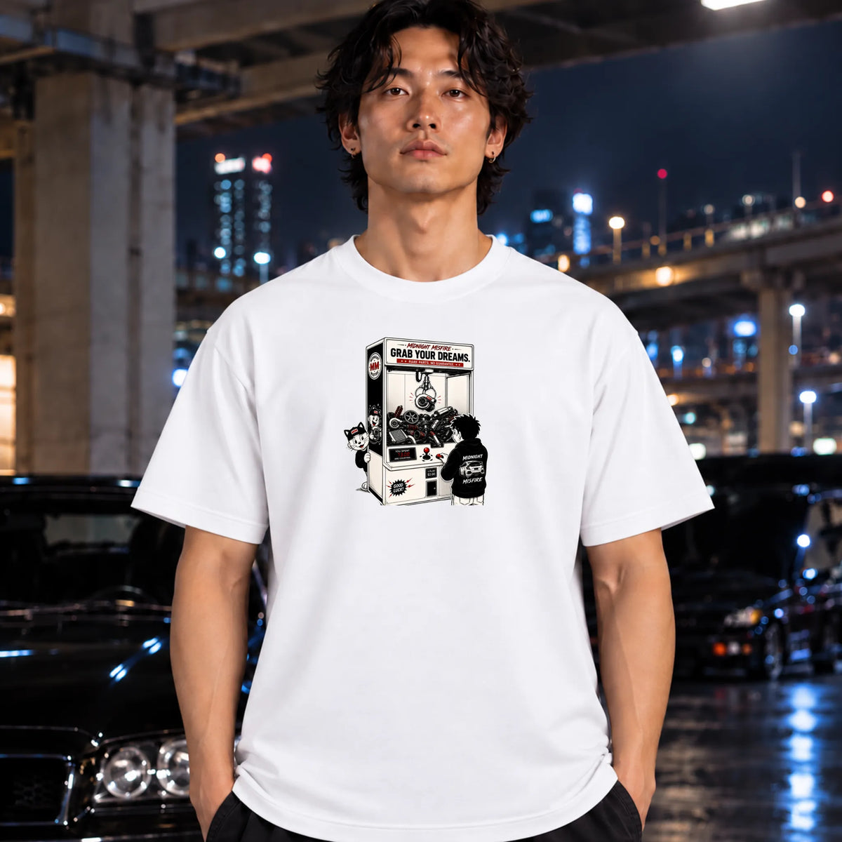 man wearing a white t-shirt featuring a black and white graphic print of a claw machine with the text 'GRAB YOUR DREAMS'.