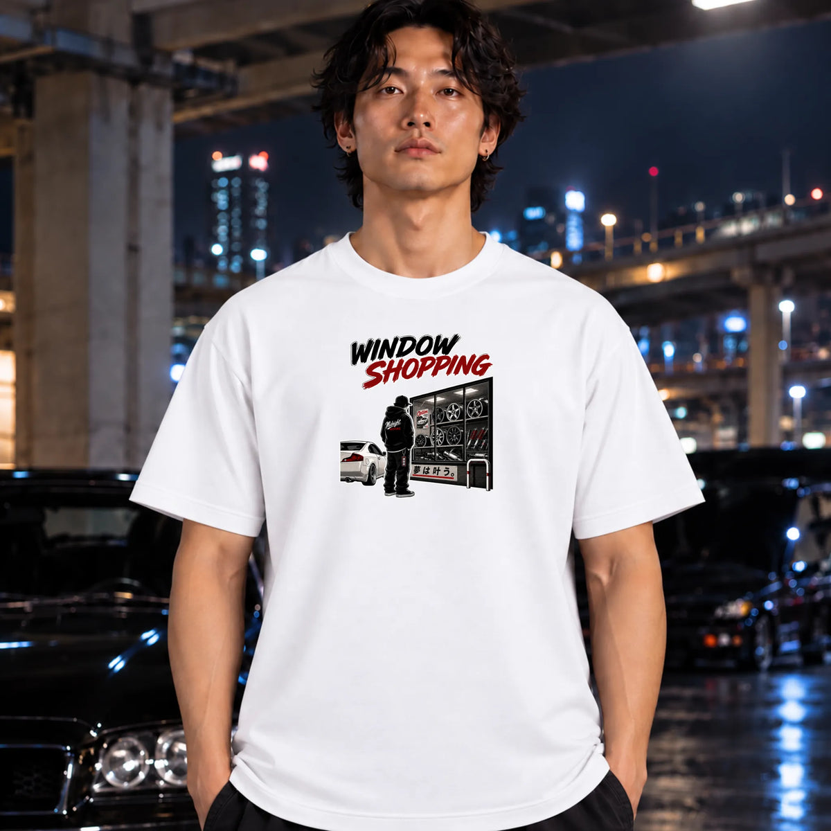 man wearing a white short-sleeved t-shirt that has a cars parked and a person checking out windows of parts.