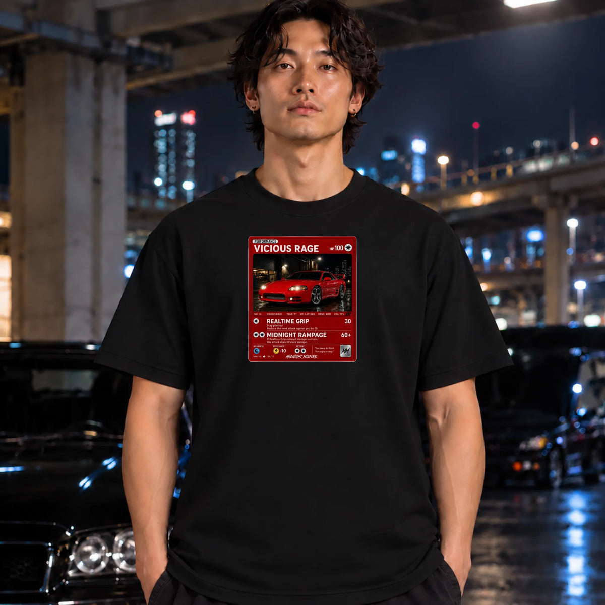A man wearing a black t-shirt with a red and white graphic print of a sports car, standing in a city street at night with blurred cars and lights in the background.