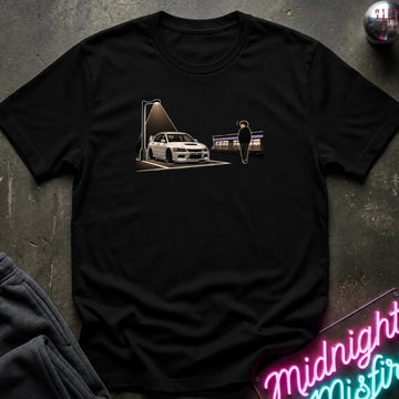 A black short-sleeve crewneck t-shirt laid flat on a dark textured surface. The shirt features a graphic print of a white sports car under a spotlight with a silhouette figure standing nearby.
