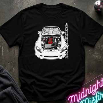 A black short-sleeve graphic T-shirt laid flat on a dark textured surface. The shirt features a white line-art illustration of a sports car with its hood open, revealing a red engine, with vertical text reading 'Late Night Intake' alongside it.