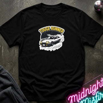 black short-sleeve t-shirt laid flat on a dark textured surface, featuring a graphic of a black sports car with the words 'TOUGE RUNNER' in yellow above it. A neon sign and folded dark fabric are partially visible around the edges.