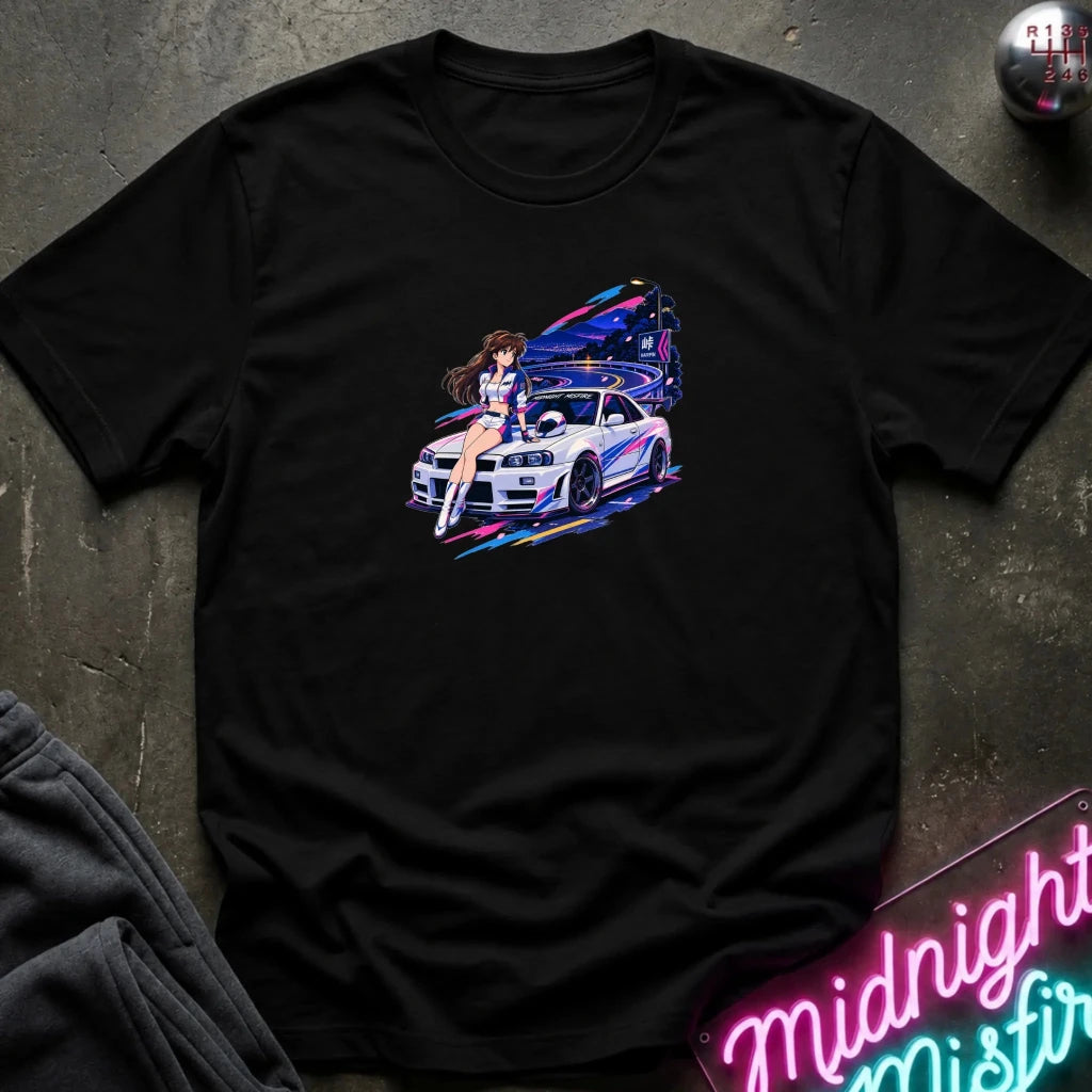 A black short-sleeve t-shirt laid flat on a dark textured surface, featuring a colorful graphic print of a white sports car and a woman in a neon-lit scene. 