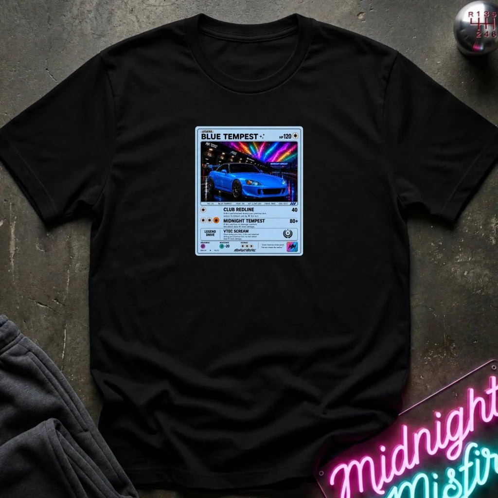 A black crewneck t-shirt laid flat on a dark textured surface, featuring a graphic print of vintage card and a car.