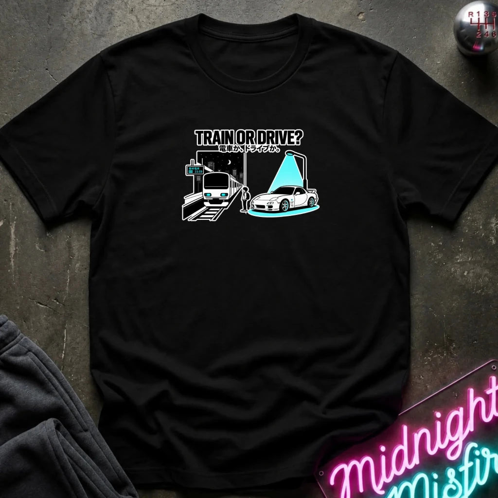 black graphic t-shirt laid flat on a dark textured surface. The graphic features a train and a car with a person.
