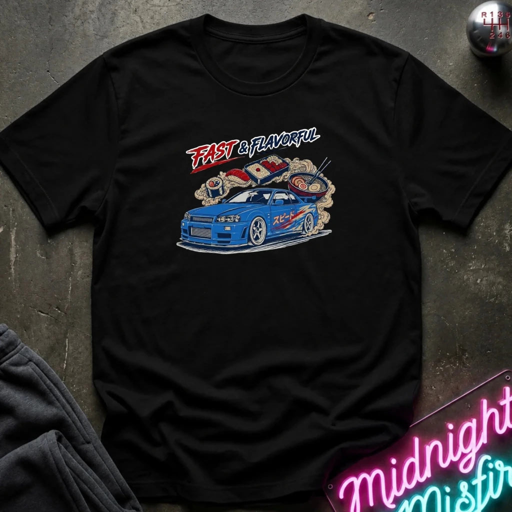 A black short-sleeve graphic t-shirt laid flat on a dark textured surface. The graphic features a blue sports car with smoke effects and the words 'FAST & FLAVORFUL' in red and white.
