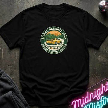 black short-sleeve t-shirt laid flat on a dark textured surface, featuring a circular graphic print of a yellow car in a scenic mountain landscape with the text 'STACE NATIONAL PARK' and 'LOWEDGED BEYOND REASON'.