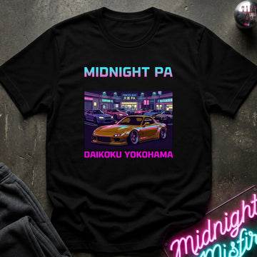 A black short-sleeve graphic T-shirt laid flat on a dark textured surface. The shirt features a colorful retro-style print with the text 'MIDNIGHT PA' at the top and 'DAIKOKU YOKOHAMA' at the bottom, surrounding an illustration of a yellow sports car in a neon-lit parking lot.