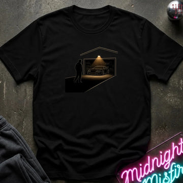 A black short-sleeve crewneck t-shirt laid flat on a dark textured surface. The shirt features a graphic print of a silhouette of a man standing in front of a lit garage with a car inside.