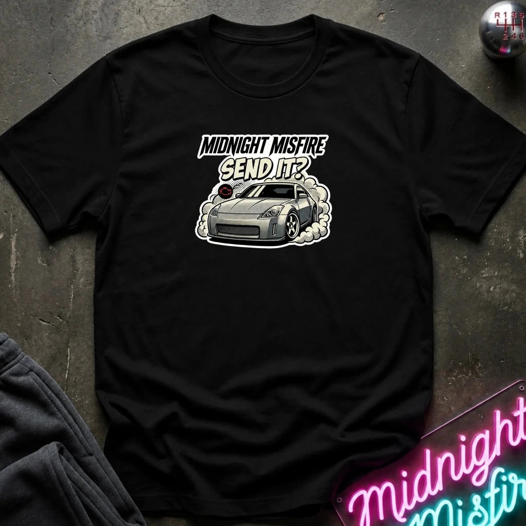 black short-sleeve t-shirt laid flat on a dark textured surface, featuring a graphic of a gray sports car with smoke and the text 'MIDNIGHT MISFIRE SEND IT?' printed on the chest.