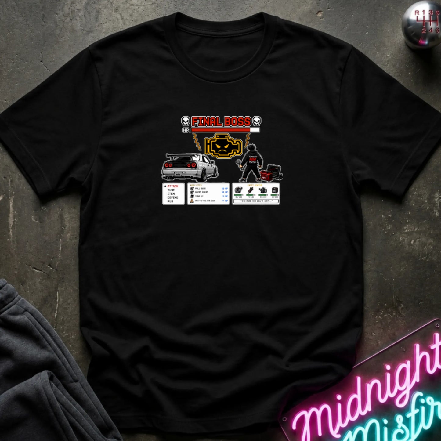A black short-sleeve crewneck t-shirt laid flat on a dark textured surface, featuring a central graphic print of a rpg character and a car. 