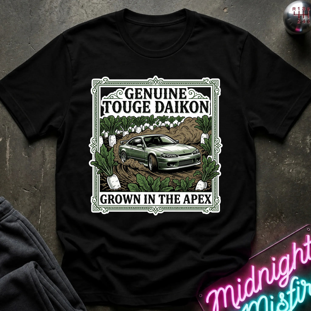 A black short-sleeve graphic T-shirt laid flat on a dark textured surface. The shirt features a large rectangular front print with the words 'GENUINE TOUGHE DAIKON' and 'GROWN IN THE APEX'.