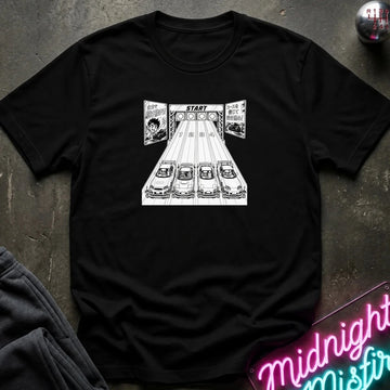A black crewneck t-shirt featuring a black and white graphic print of 4 cars lined up at a race starting line with the word 'START' above them. The shirt is laid flat on a dark textured surface with a neon sign and dark pants partially visible in the corners.