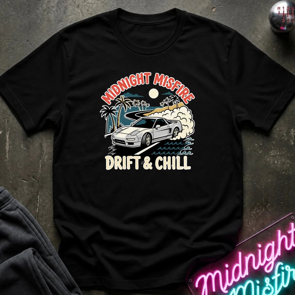 A black short-sleeve graphic t-shirt laid flat on a dark textured surface. The shirt features a retro-style print of a white sports car drifting with palm trees, smoke, and the text 'MIDNIGHT MISFIRE' and 'DRIFT & CHILL'.