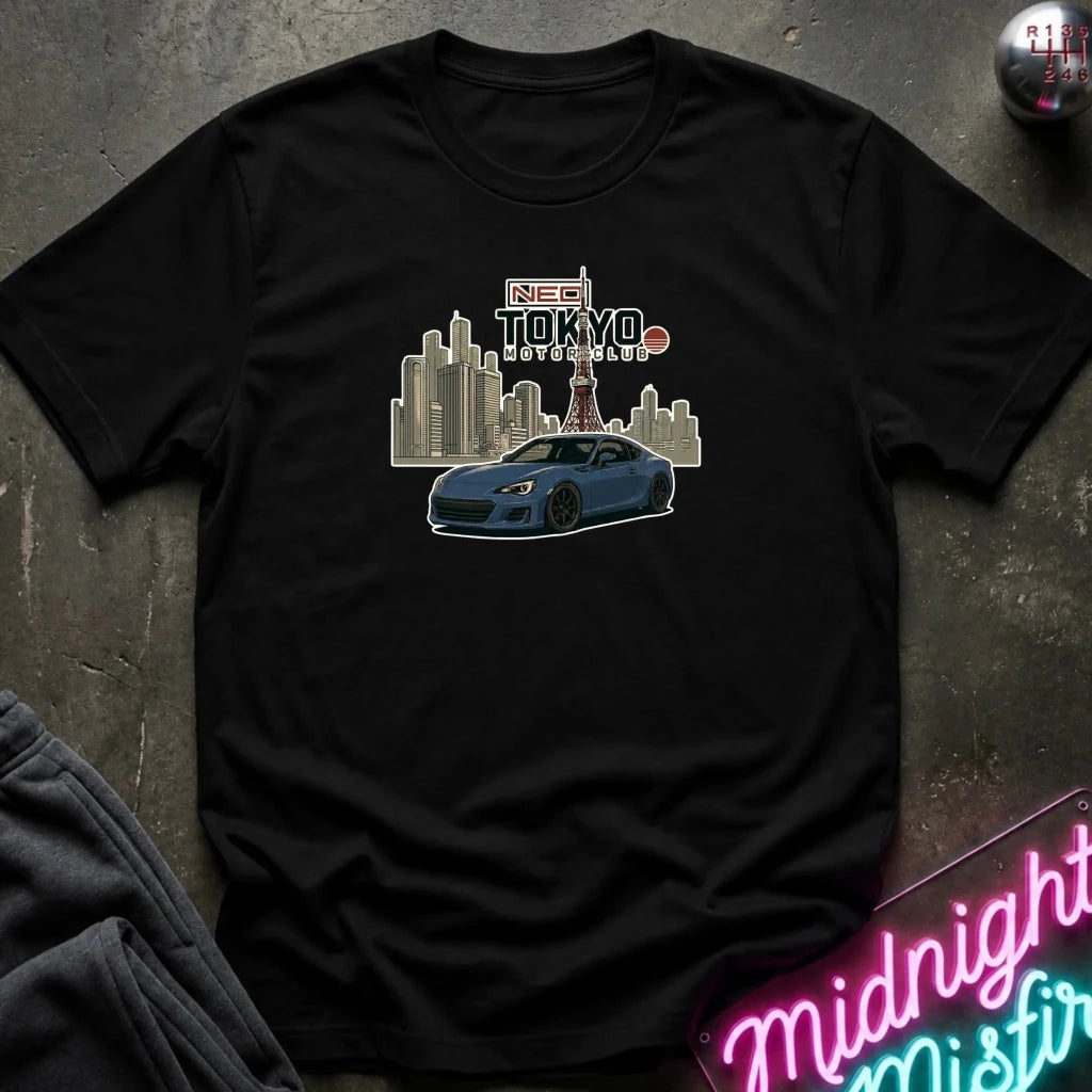 A black short-sleeve graphic t-shirt laid flat on a dark textured surface. The graphic features a blue sports car in front of a stylized Tokyo skyline 