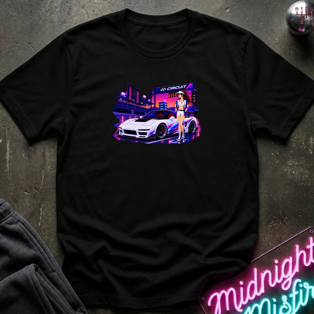A black  short-sleeve t-shirt laid flat on a dark textured surface, featuring a colorful graphic print of a white sports car and a woman in a neon-lit scene. 
