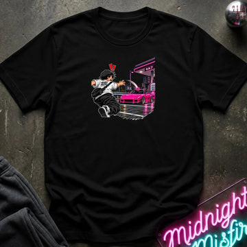 A black short-sleeve crewneck t-shirt laid flat on a dark textured surface. The center of the shirt features a graphic print of an anime character in a black and white outfit with a hat, next to a sports car 