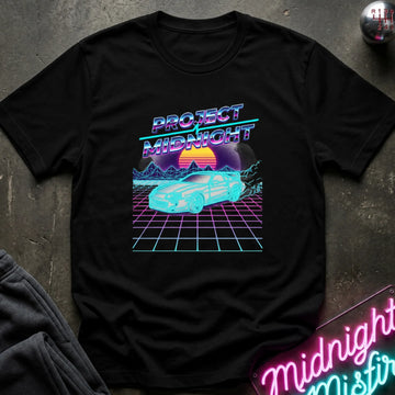 A black short-sleeve t-shirt with a retro 80s synthwave graphic reading 'PROJECT MIDNIGHT' above a glowing cyan car on a purple grid with a sunset, laid flat on a dark textured surface with a neon sign and folded gray fabric nearby.