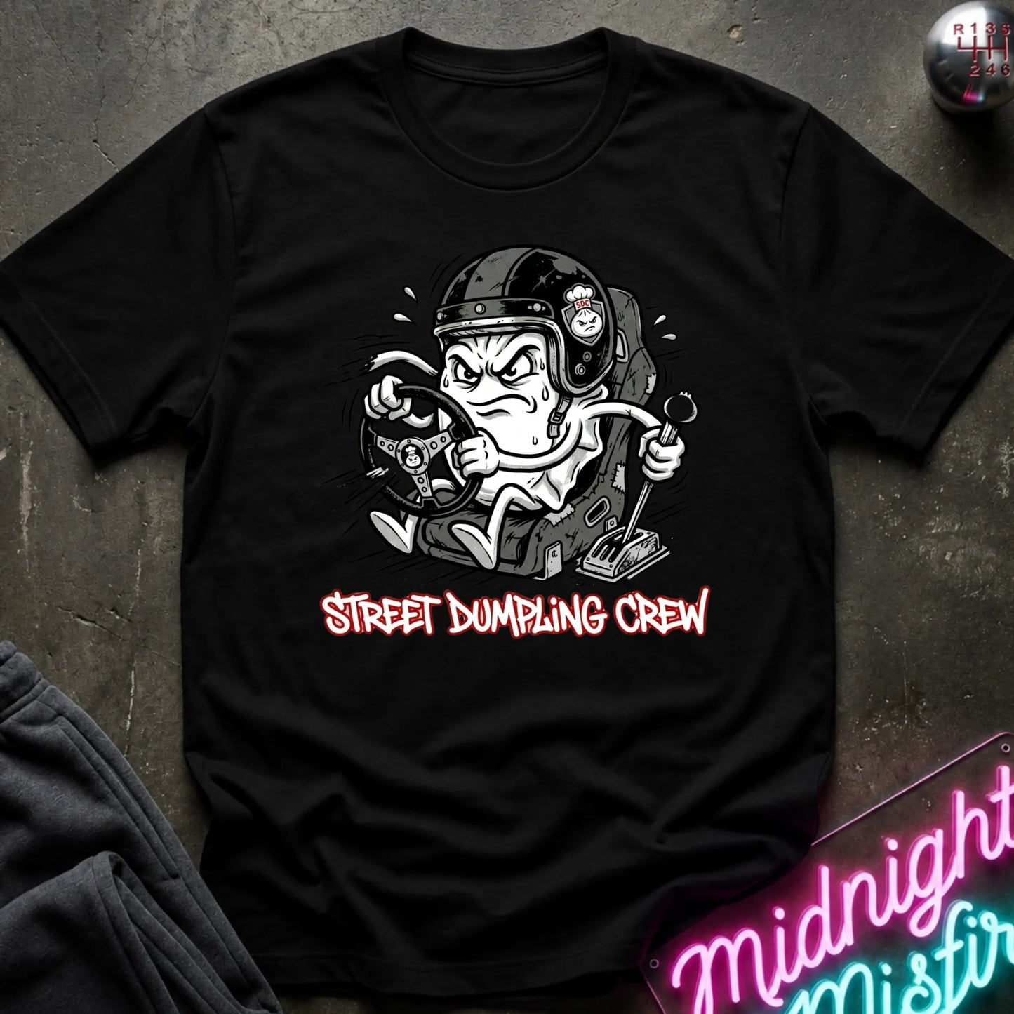 A black graphic t-shirt laid flat on a dark textured surface. The shirt features a cartoon illustration of a street-dumping character in a helmet with the text 'STREET DUMPING CREW' printed below in red and white.