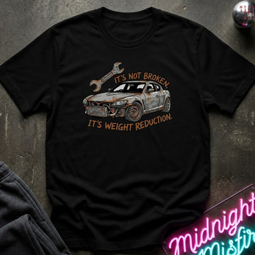 A black short-sleeve graphic T-shirt laid flat on a dark textured surface. The shirt features a distressed illustration of a car with a wrench and the text 'IT'S NOT BROKEN.