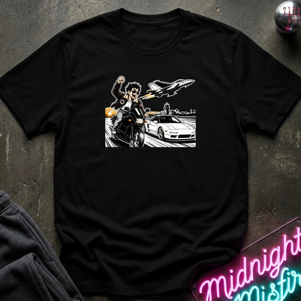 A black short-sleeve crewneck t-shirt laid flat on a dark textured surface, featuring a black and white graphic print of a motorcycle racer, a sports car, and a jet plane.
