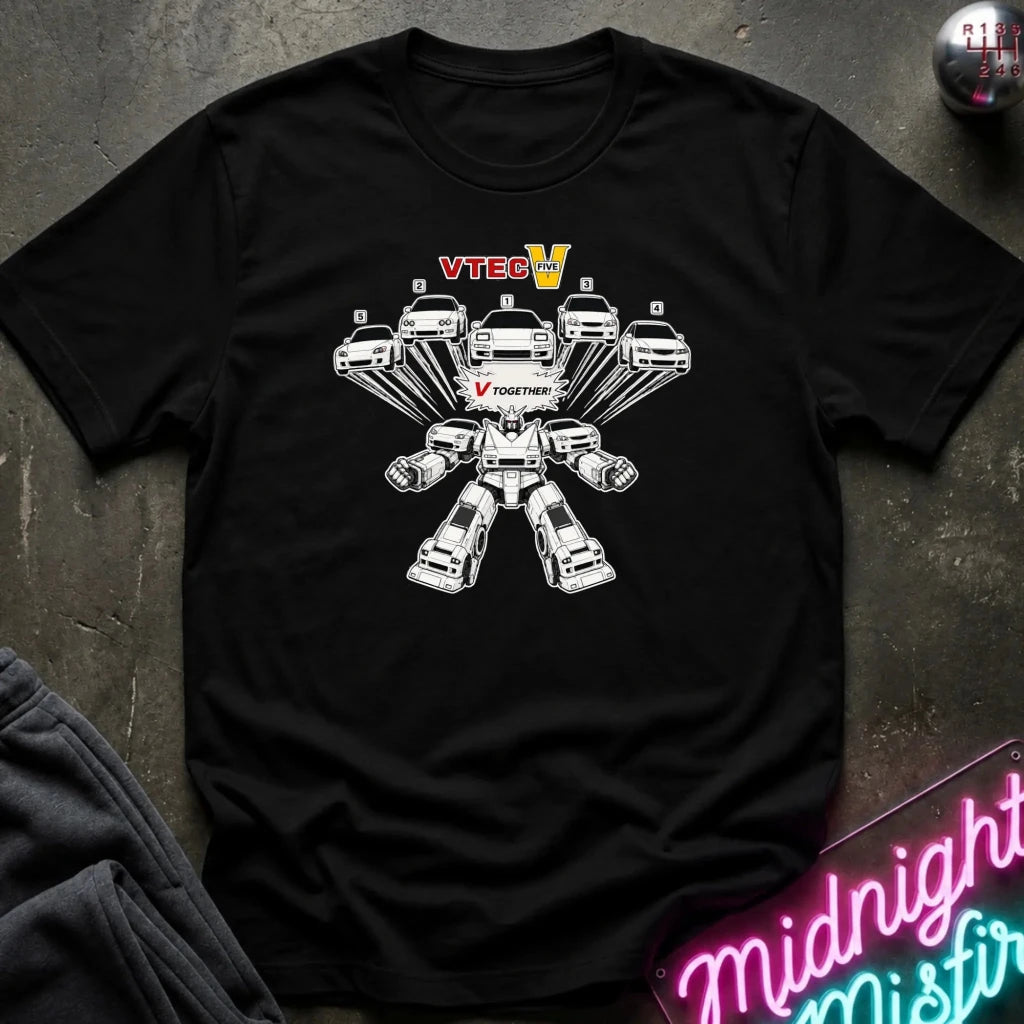 A black short-sleeve graphic t-shirt laid flat on a dark textured surface. The shirt features a white line-art graphic of a multi-axle vehicle transforming into a robot
